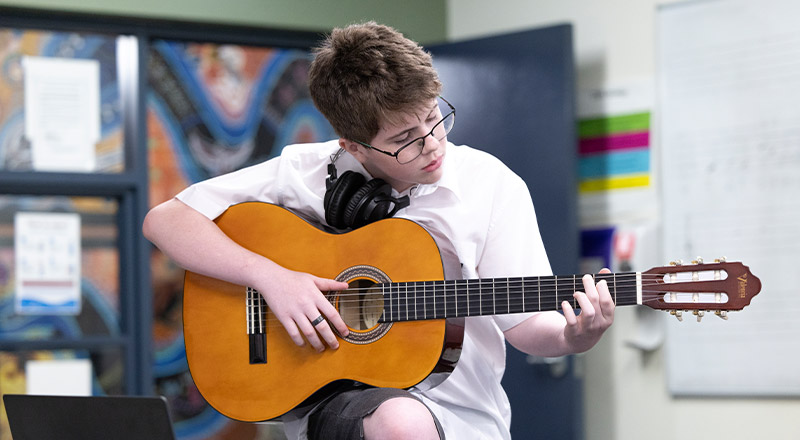 Student playing the guitar in the classroom at Xavier College Llandilo