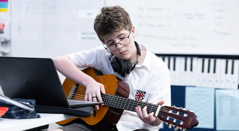 Student learning to play the guitar in the classroom at Xavier College Llandilo