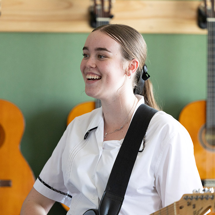 Student playing the guitar in the music room at Xavier College Llandilo