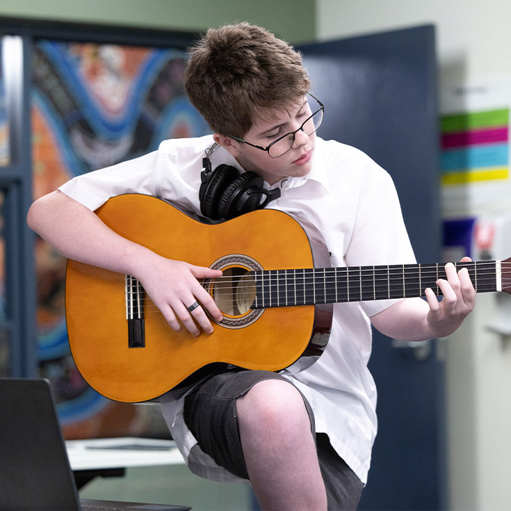 Student practising guitar in the classroom at Xavier College Llandilo