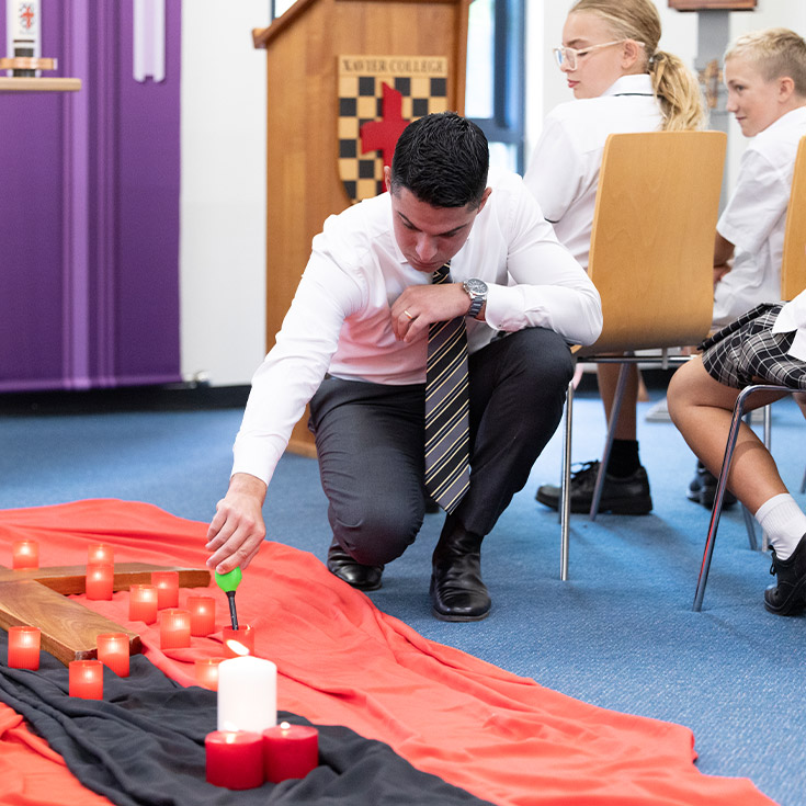 Teacher lighting a candle during a liturgy at Xavier College Llandilo